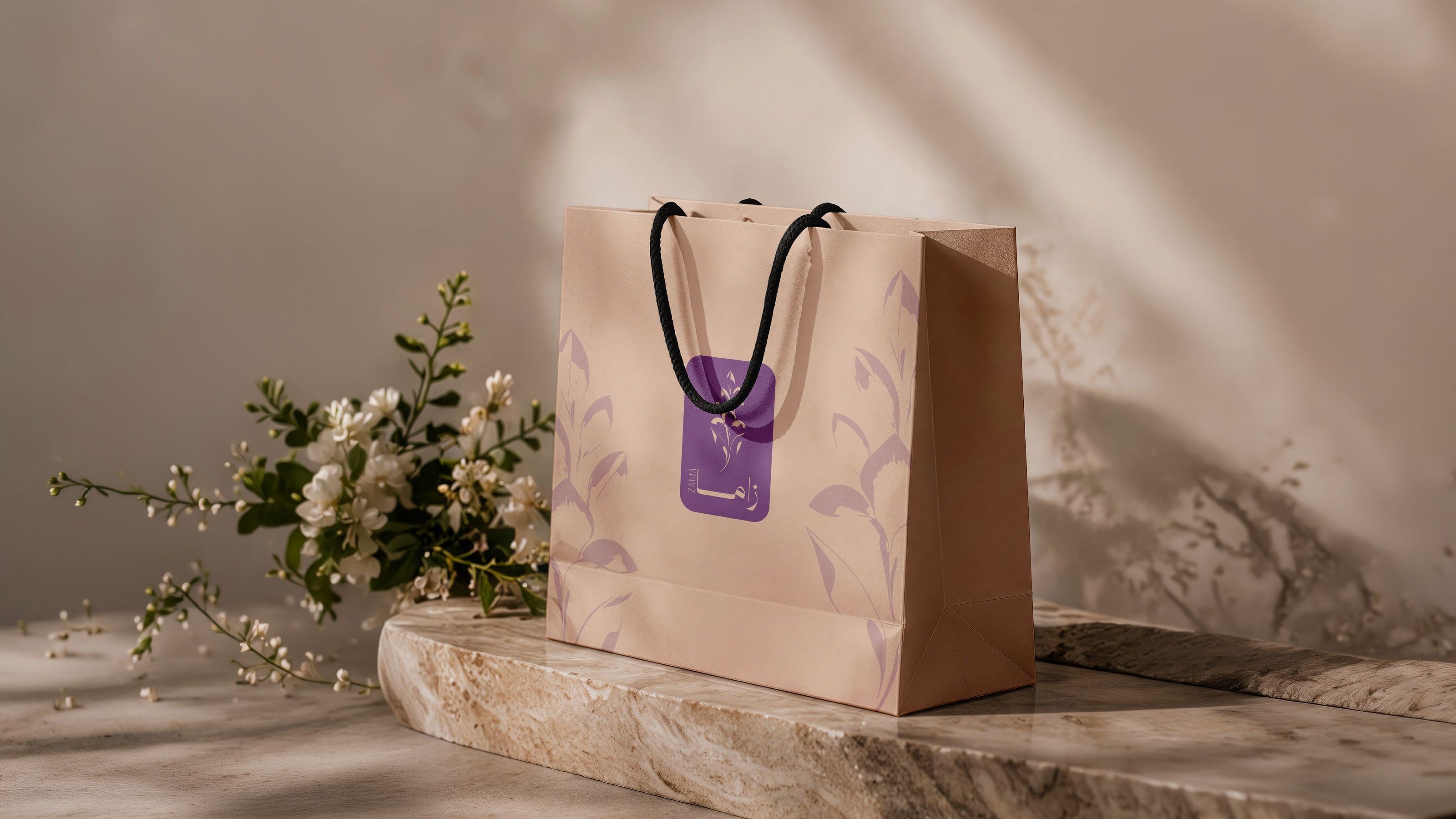 Zama's peach gift bag on a travertine block beside a sprig of jasmine